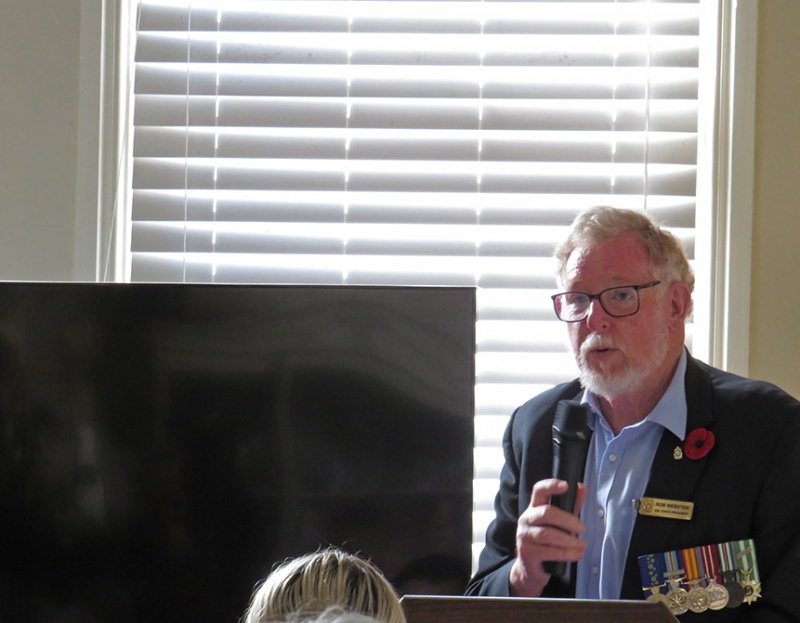 Dr Robert Webster wearing his military medals and a poppy, holding a microphone as he opens the resource centre